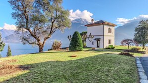 A white building with a red roof, surrounded by trees and a lake, with mountains in the background. - Stunning private villa for 4 guests with WIFI, TV and patio (Calozzo)
