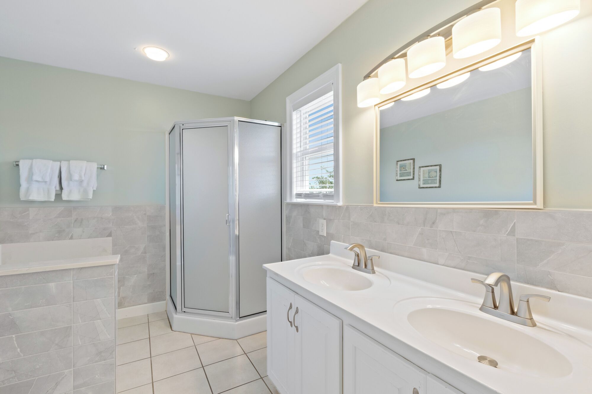 A bathroom with a walk-in shower, two sinks, a large mirror, and a window with blinds.
