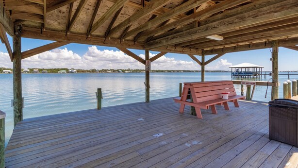A wooden pier with a bench and a trash bin, overlooking a calm body of water with a distant shoreline.