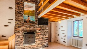 A room with a stone fireplace, wooden beams, a large window, and a black leather sofa. - Wonderful private villa for 6 guests with WIFI, TV and patio (Calozzo)