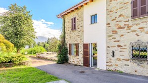 A stone building with a paved driveway, a small garden, and a view of the mountains. - Wonderful private villa for 6 guests with WIFI, TV and patio (Calozzo)