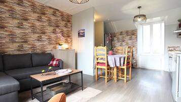 Een moderne woonkamer met een bank, eettafel, stoelen en een keukenhoek.