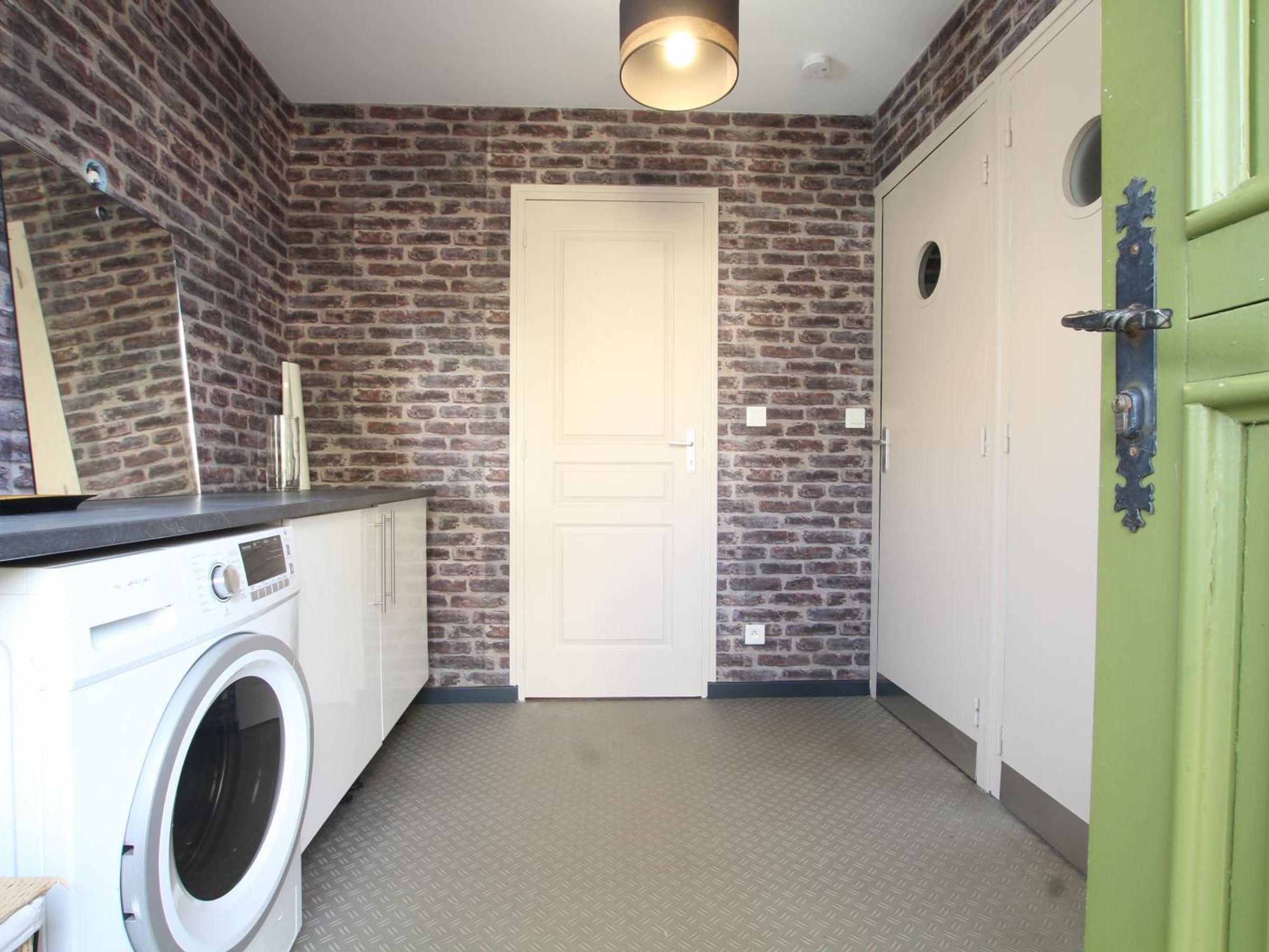 A laundry room with a washing machine, a dryer, a brick wall, a white door, and a green door.