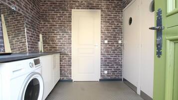A laundry room with a washing machine, a dryer, a brick wall, a white door, and a green door.
