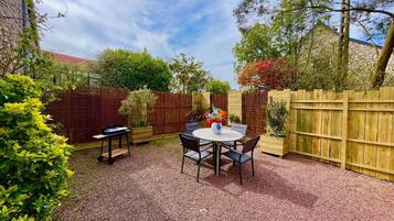 A patio area with a round table and chairs, surrounded by wooden fences and greenery.