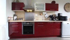 Une cuisine moderne avec des meubles de couleur rouge, des appareils électroménagers en acier inoxydable et une horloge au mur.