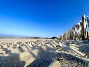 Une plage de sable bordée d’une clôture en bois, sous un ciel bleu et dégagé.