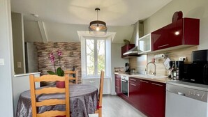 Une cuisine moderne avec un coin repas, dotée d’un pare-feu en pierre, de meubles de rangement rouges et d’un four encastré.