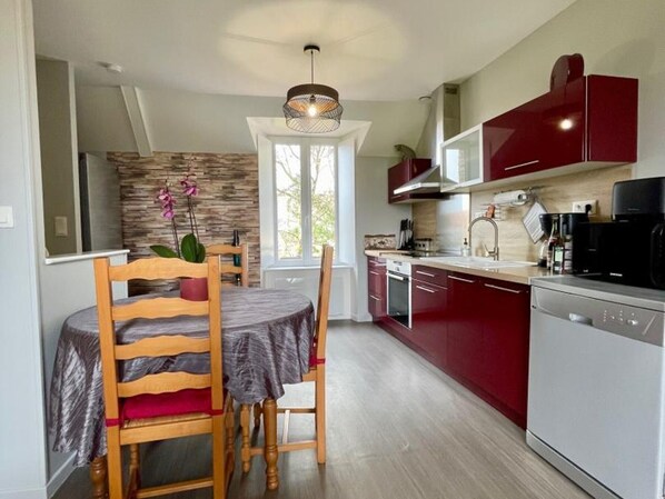 Une cuisine moderne avec un coin repas, dotée d’un pare-feu en pierre, de meubles de rangement rouges et d’un four encastré.