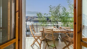 Un balcon avec une table et des chaises en bois, une plante en pot et une bouteille de vin.