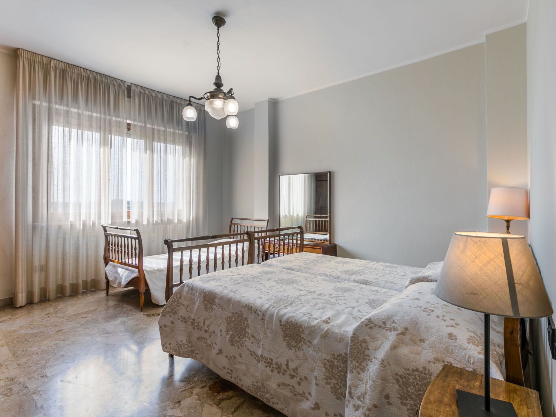 A bedroom with a bed, a chair, a desk, a lamp, and a mirror.