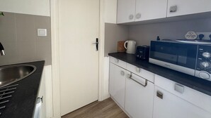 Una cocina compacta con armarios blancos, una encimera negra, un microondas y una cafetera.