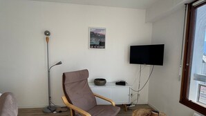 Una sala de estar moderna con un sillón de cuero marrón, una mesa de centro redonda de madera, un mueble blanco, una lámpara de pie y un televisor de pantalla plana montado en la pared.