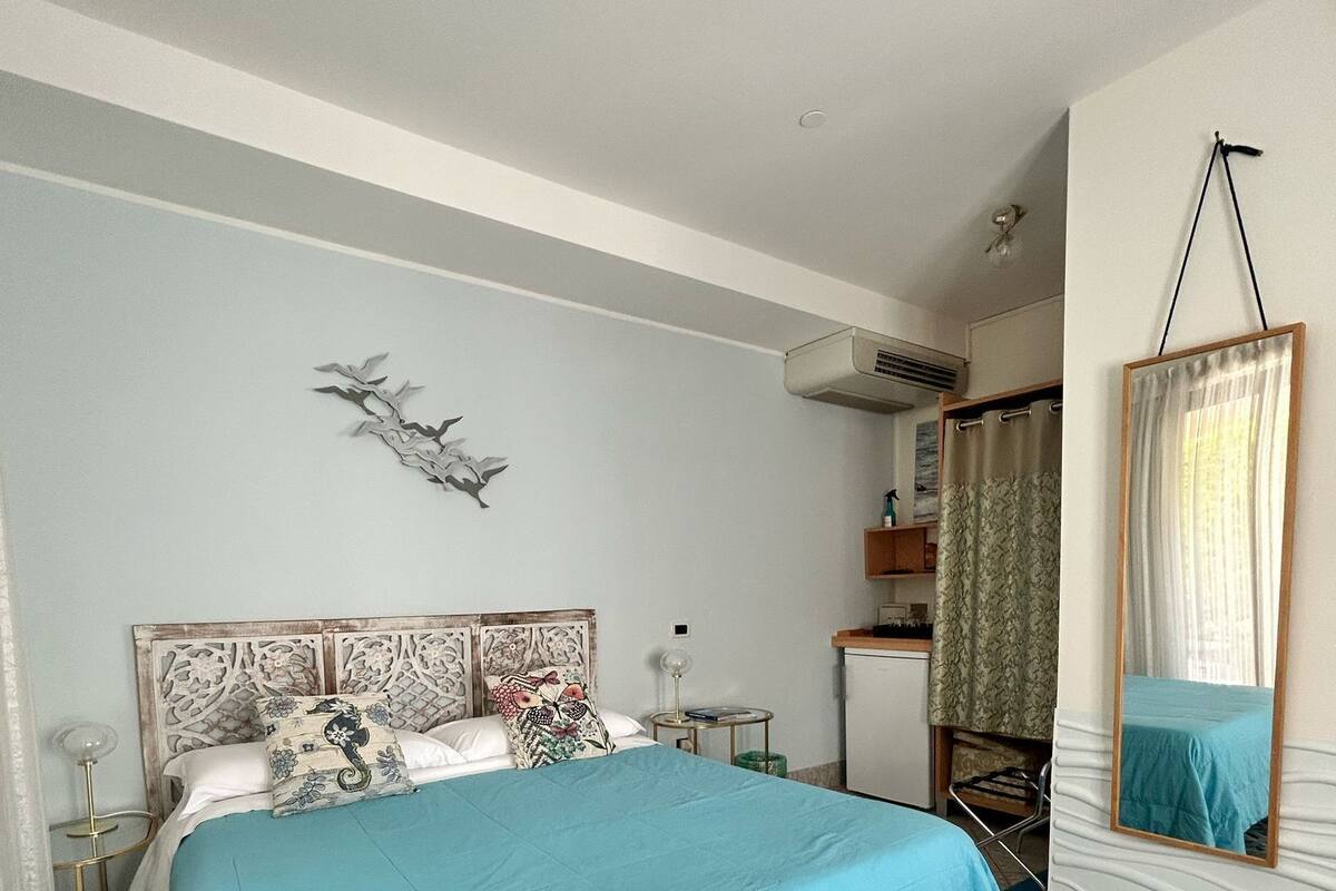 Een slaapkamer met een groot bed, een klein nachtkastje, een wandairconditioner en een badkamer met douchegordijn.