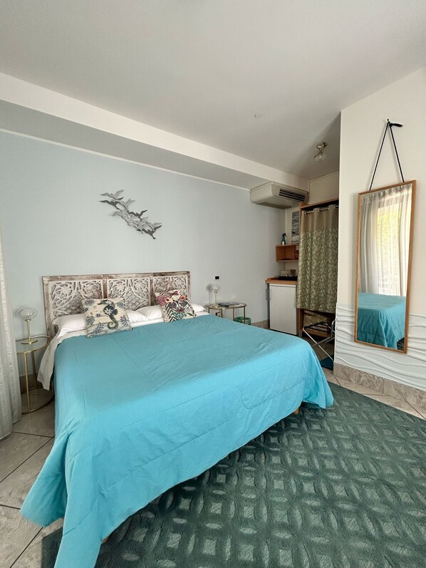 A bedroom with a large bed, a small bedside table, a wall-mounted air conditioner, and a bathroom with a shower curtain. - Casa di Carlo Goldoni (Chioggia)