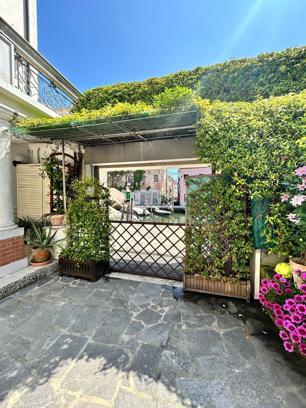 A gated entrance with a metal gate, potted plants, and a stone-paved area leading to a building with a balcony. - Casa di Carlo Goldoni (Chioggia)