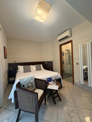 Ein Hotelzimmer mit Bett, Stuhl, kleinem Tisch, Klimaanlage und Spiegel.