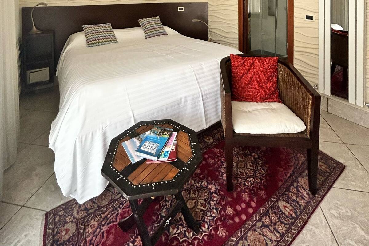 Een slaapkamer met een bed, een stoel, een klein tafeltje, een airconditioning en een spiegel.
