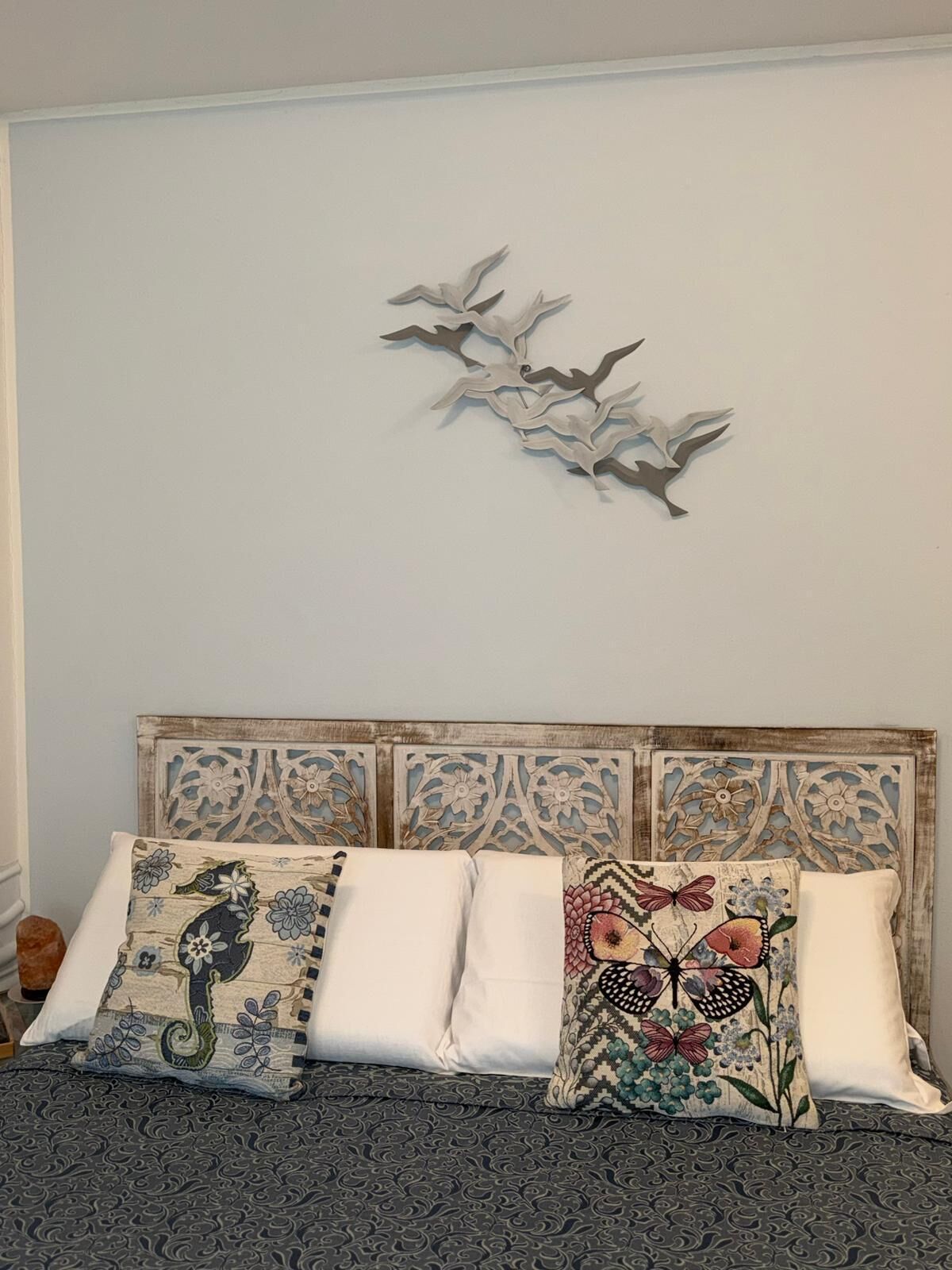 Un lit avec une literie à motifs et deux coussins décoratifs, une tête de lit ornée de motifs sculptés et une œuvre d’art abstraite accrochée au mur.