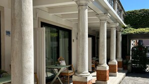 Un bâtiment doté d’un espace extérieur couvert, soutenu par des colonnes, et caractérisé par un sol carrelé et une base en briques.