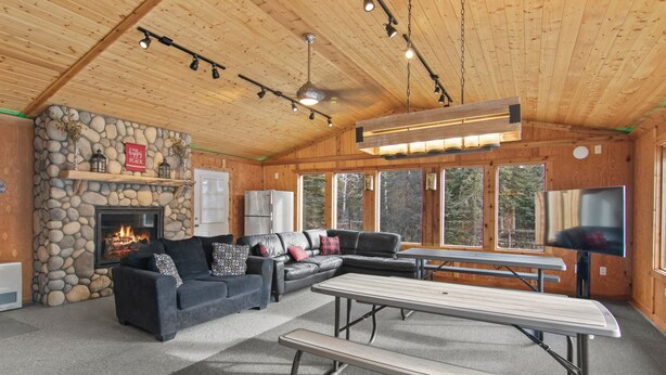 Un interior de cabaña acogedor, con chimenea de piedra, sofá seccional, mesa de comedor y televisor.