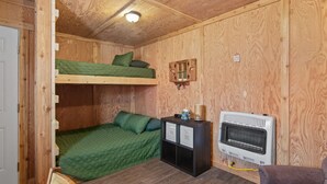 Una habitación pequeña de madera con literas, un calentador y un mueble bajo con cajones.