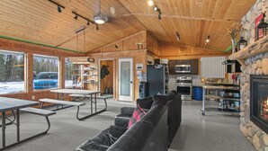 A cabin interior with a stone fireplace, kitchen area, and seating. - Silver Cabin – Dry Cabin with Bunks | Fish On! (Sterling)
