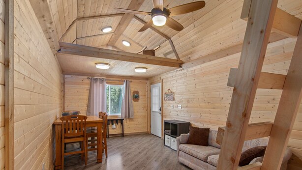 Ein gemütliches Blockhaus-Interieur mit Essbereich, einer Couch, einem Deckenventilator und einem Kamin.