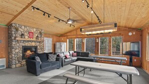 A cozy cabin interior with a stone fireplace, a sectional sofa, a dining table, and a television. - King Cabin -Full Kitchen + Laundry | Kenai Retreat (Sterling)