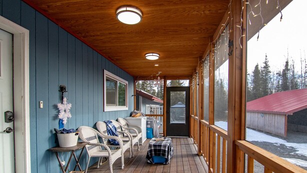 A covered porch with wicker chairs, a small table, and a bench. - King Cabin -Full Kitchen + Laundry | Kenai Retreat (Sterling)