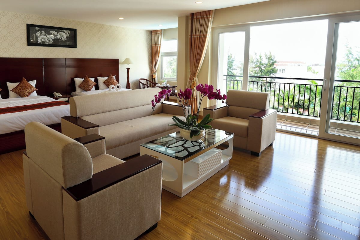 Habitación de hotel con una cama grande, un sofá, una mesita de centro y un balcón con vistas.
