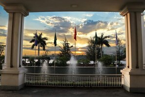 Una fuente bajo una pérgola con banderas, palmeras y vistas al atardecer.