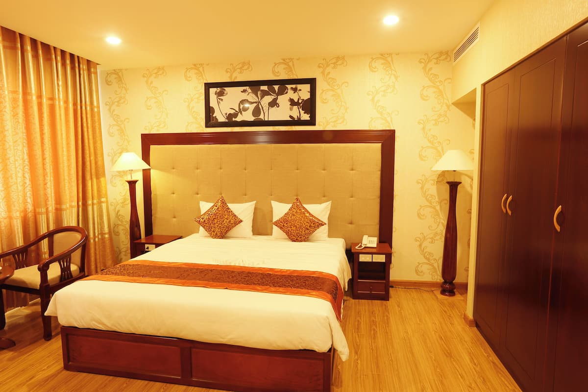 Una habitación de hotel con una cama grande, dos mesitas de noche, una silla, un armario y un adorno de pared.