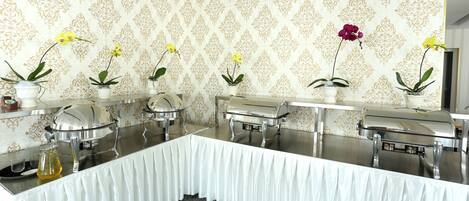 A buffet setup with multiple serving stations, each with a covered dish and a potted plant.