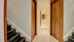 Um corredor de hotel moderno com piso de mármore, portas de madeira e uma escadaria.