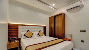 Quarto de hotel moderno com uma cama grande, cabeceira de madeira, mesas de cabeceira e um aparelho de ar condicionado.