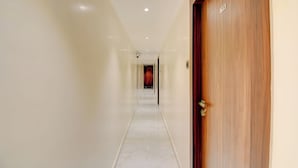 Um corredor com uma porta de madeira à direita e uma parede branca à esquerda.