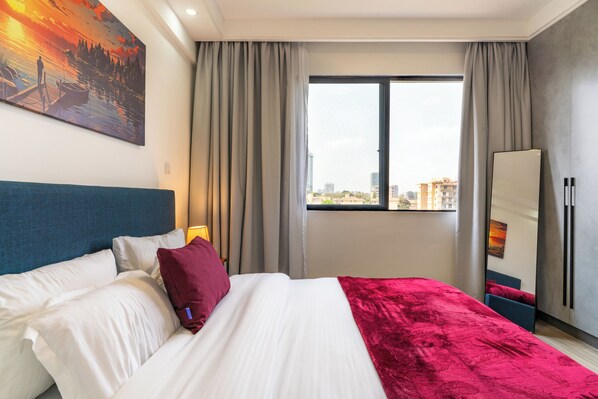 A hotel room with a bed, a large window, a painting on the wall, and a wardrobe.