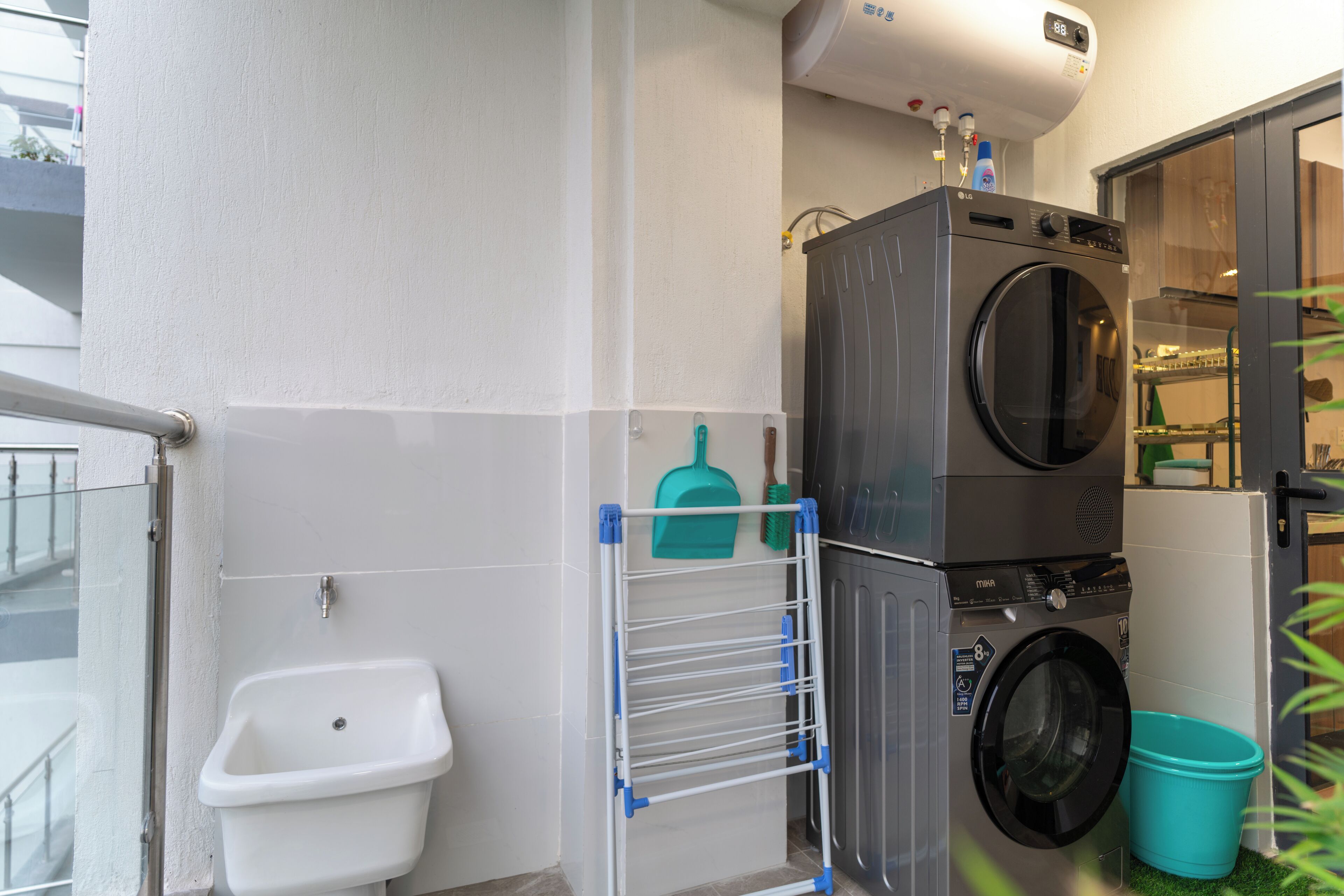 Un espace réduit dédié à la buanderie, comprenant un lave-linge, un étendoir, un évier et une petite poubelle.