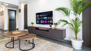 A modern living room with a flat-screen TV mounted on the wall displaying various streaming services. There is a wooden coffee table with a woven basket, a potted plant, and a grey entertainment unit below the TV. - Skyline symmetry (Nairobi)
