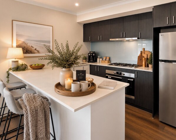 A modern kitchen with dark cabinets, a central island, bar stools, a coffee machine, and a refrigerator.