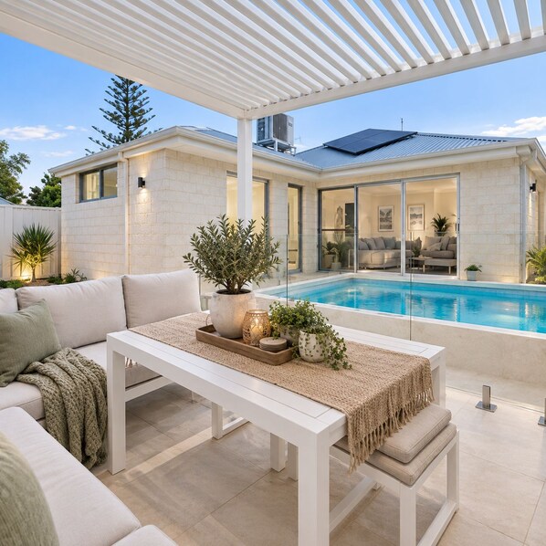 A modern outdoor living area with a pool, white furniture, and a pergola.
