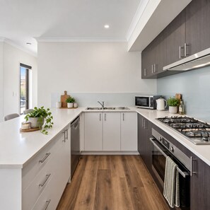 A modern kitchen with a white countertop, stainless steel appliances, and wooden flooring.