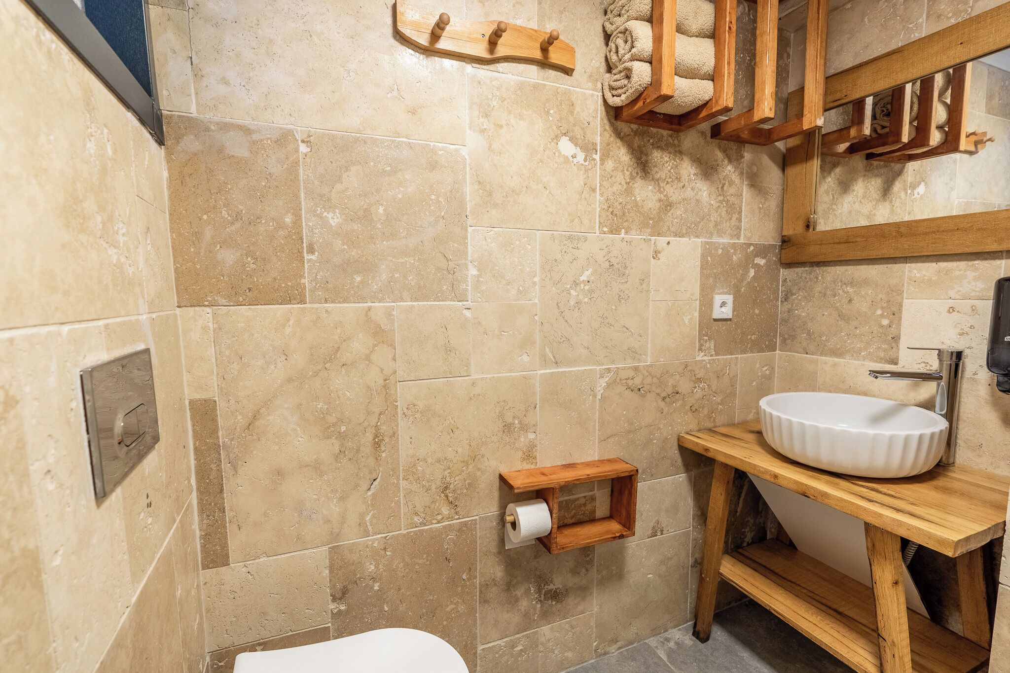 A bathroom with beige tiled walls, a wooden vanity with a sink, and a toilet.