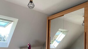Makuuhuone, jossa on kattovalokuvio, kuviollinen päiväpeite sängyllä, pieni silityspiste ja peilillä varustettu vaatekaappi.