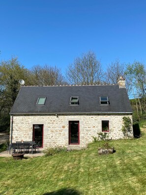 A stone building with a sloped roof, two windows, and a chimney.