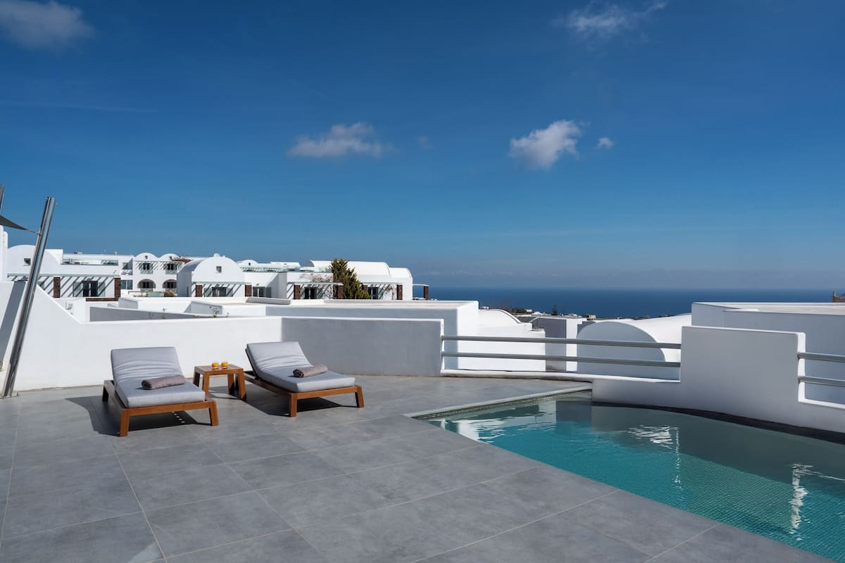A rooftop pool area with two lounge chairs and a small table, overlooking a coastal cityscape.