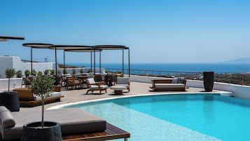 A rooftop infinity pool with lounge chairs and umbrellas, overlooking a coastal landscape.