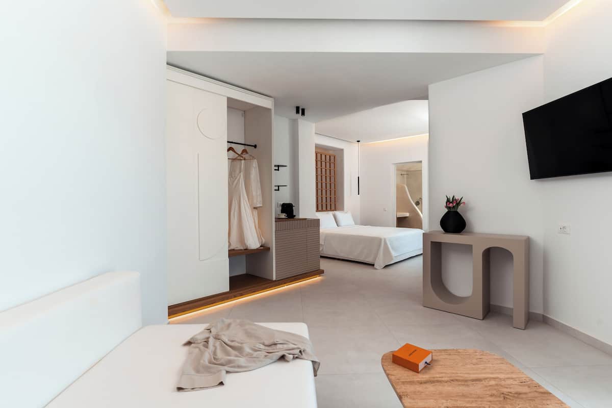 A modern hotel room with a bed, a seating area, a wardrobe, and a TV mounted on the wall.