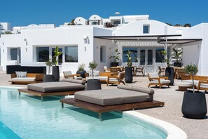 A pool area with lounge chairs, a pergola, and a view of white buildings. - Oikos Santorini Living Concept (Santorini)